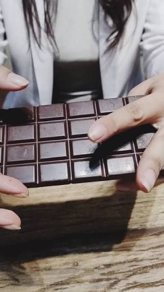 Manos partiendo una tableta de chocolate sobre una mesa de madera